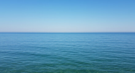 Fototapeta premium Tranquil seascape featuring a calm, blue ocean meeting a clear, cloudless sky on a bright, sunny day.