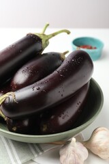 Many wet ripe eggplants and garlic on white table, closeup