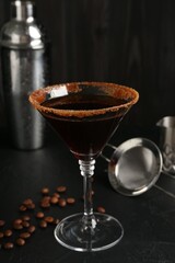Martini cocktail with sugar in glass, coffee beans and shaker on black table, closeup