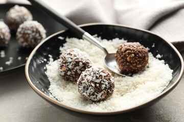 Making tasty chocolate candies with nuts and coconut flakes at light table, closeup