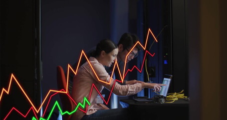 Two IT professionals wearing badges analyzing data in control room, with laptops and yellow cables