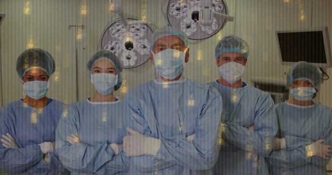 Standing medical team wearing blue gowns and masks in operating room with digital currency overlay - Powered by Adobe