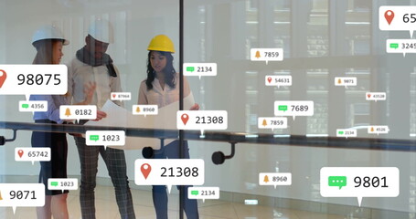 Reviewing team wearing safety helmets discussing blueprint on glass railing, atrium, floating icons