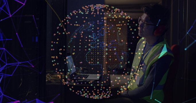 Tech wearing safety vest and headphones monitoring servers in server room, with globe, copy space