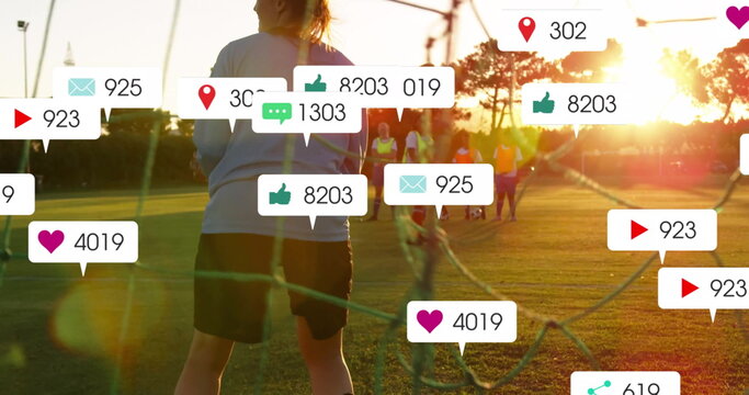 Defending goalkeeper wearing top and shorts guarding net on grass with neon bibs and social icons