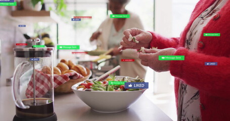 Senior woman in red cardigan tearing lettuce into salad bowl in kitchen, social icons, copy space