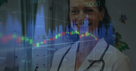 Standing doctor wearing white coat and stethoscope in clinical room showing financial chart overlay