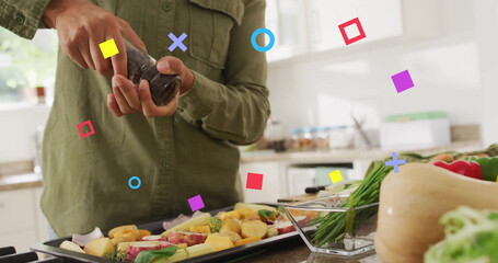 Seasoning home cook holding pepper grinder over baking tray at kitchen countertop, with fresh herbs
