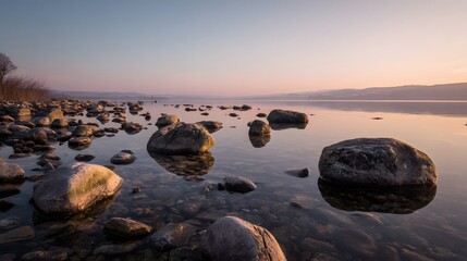Obraz premium Serene lake view with reflective rocks at dawn, capturing the tranquil beauty of nature's gentle transition into a new day.