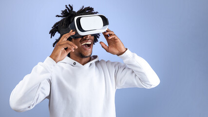 Funky Afro teen guy wearing VR headset, exploring cyberspace, using virtual reality for entertainment on violet studio background. Cool black adolescent experiencing modern technologies