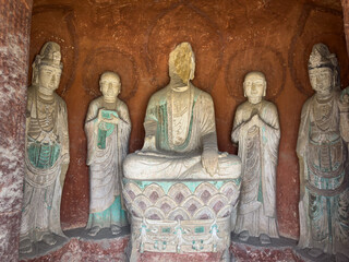 Statues of Buddha with broken head, Disciples, Bodhisattvas in a grotto at Thousand-Buddha Cliff along bank of Jialing River in Guangyuan, Sichuan, China, constructed from late Northern Wei Dynasty.