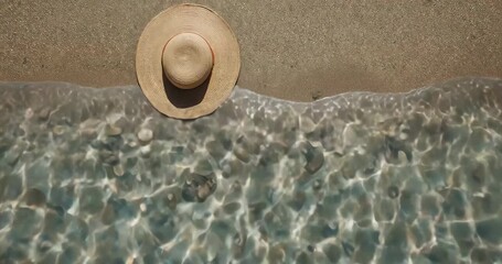 Gentle waves lapping straw wide-brimmed sunhat on wet golden sand, creating shimmering patterns - Powered by Adobe