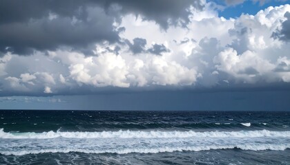 Fototapeta premium Ocean waves crash on the shore under dramatic storm clouds with a glimpse of blue sky