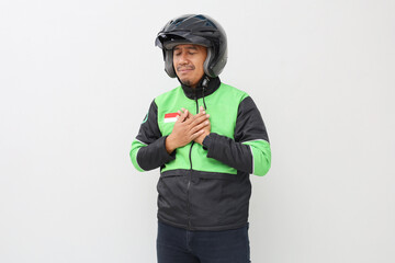Relieved Asian online taxi driver wearing green jacket and helmet holding his chest