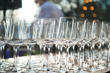Many clean wine glasses aligned outdoors in daylight; catering setup before guests arrive.