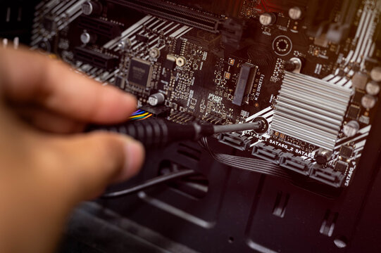 Technician hand using screwdriver to install or fix computer motherboard inside PC case, showing computer repair, building or hardware upgrade process in close-up detail.
