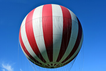 red and white gas filled huge balloon. light blue sky. popular attraction in Budapest city park. summer lights. travel, tourism, leisure and outdoors. low angle closeup view.