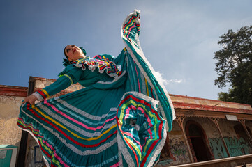 Mexican folk dancer performing in turquoise traditional dress with colorful ribbons outdoors