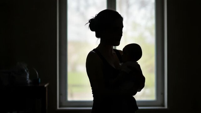Silhouette of mother holding her baby in front of a window