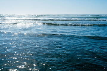 Small waves rolling in the shallow water out to the horizon on a clear blue calm day.
