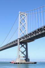 Puente colgante de acero sobre la bahia con barco rojo en el agua.