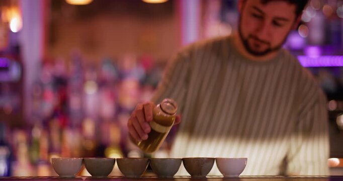 Barman pouring liquid. Asian pub. Male bartender filling portioned small ceramic cups for sake. Man serving traditional japanese alcoholic order.