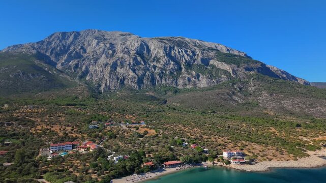 Scenic coastal village of Paralia Limnionas with colorful houses by the sea and majestic mountains rising behind, Samos Island