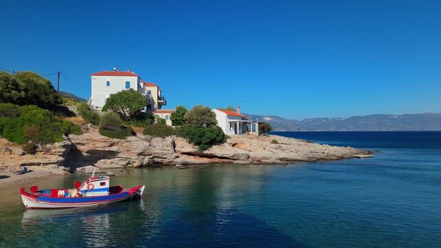 Picturesque fishing village atmosphere in Paralia Limnionas, Samos, with a red-blue boat and Mediterranean coastal homes