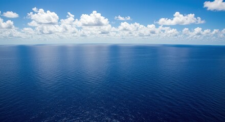 Obraz premium A vast expanse of deep blue ocean meets a serene sky filled with fluffy white clouds.