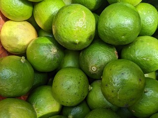 Top-down shot of a pile of fresh limes and a few lemons. The image focuses on the vibrant green and yellow colors and the textured skin of the citrus fruits