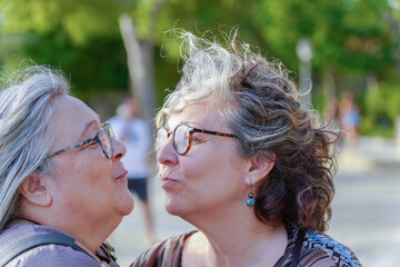 Two senior women are expressing their love and affection with a gentle kiss in a park setting...