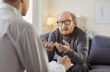 Serious senior patient consulting psychologist during therapy session in office, seeking aid and treatment, fostering a focused visit for mental health support within a structured.