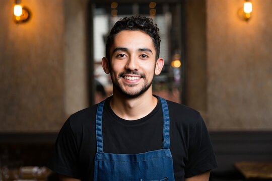 Portrait of a smiling bartender in a restaurant wearing an apron and a black t shirt shirt