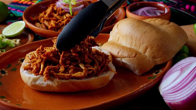 Mexican food, preparing a Mexican torta sandwich, serving on top sherred cochinita pibil meat