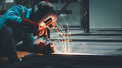 A skilled worker practices welding techniques, producing bright sparks while shaping metal materials. This activity takes place in an industrial workshop during the evening hours
