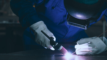 A skilled worker focuses intently while using a welding torch to fuse metal components together in a workshop setting. The precision of the task highlights craftsmanship