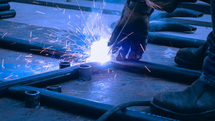 A skilled worker is welding metal pieces together, creating bright sparks in an industrial workshop. The scene showcases the focus and technique required for precision craftsmanship
