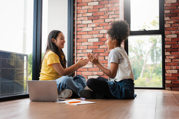 Diverse girls playing a hand clapping game on the floor in a bright room, Young friends enjoying a fun moment together, sitting by a window in a modern home