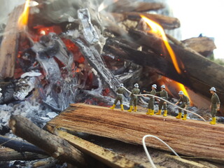 Mini toy of action figure at table with blurred background. Miniature photography concept design. Minifigure of fire fighter crew character with wood and fire.