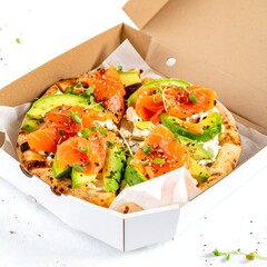 Open pizza box with two slices of salmon and avocado flatbread