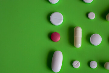 Randomly arranged colorful pills and capsules on a bright green background. This macro shot emphasizes the texture and shape of the medications. 