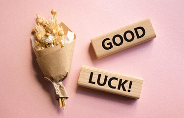 Good luck symbol. Wooden blocks with words Good luck. Beautiful pink background with bouquet of...