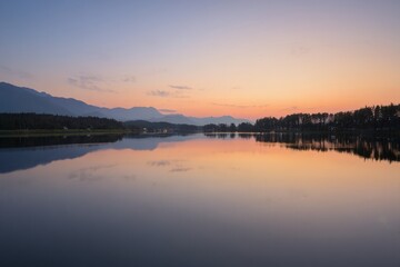 Fototapeta premium Serene lake landscape at sunset with mountain backdrop and tranquil water reflections