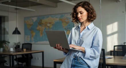 Young Professional Woman in a Modern Office Setting Working on a Laptop Computer with a World Map in the Background