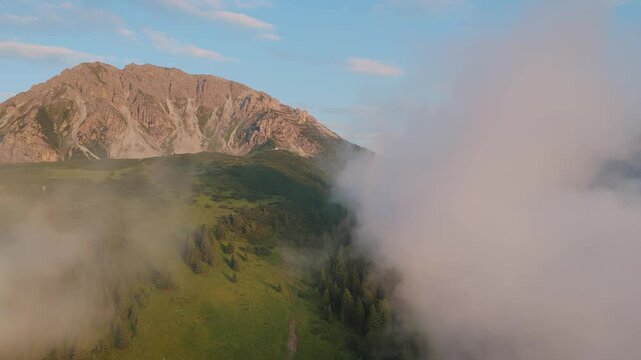 Flying through clouds to reveal a green mountain valey in the Alps.
