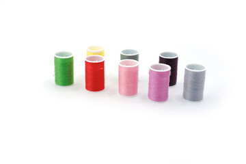 Studio photo of several small spools with multicolored sewing threads, arranged on a clean white background