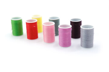 Studio photo of several small spools with multicolored sewing threads, arranged on a clean white background