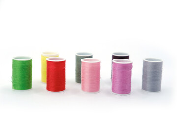 Studio photo of several small spools with multicolored sewing threads, arranged on a clean white background