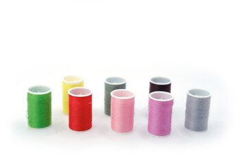 Studio photo of several small spools with multicolored sewing threads, arranged on a clean white background