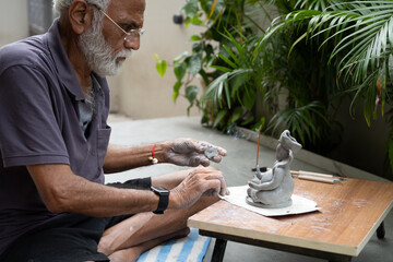 Indian old man crafting an eco-friendly clay Ganesh idol for Ganesh Chaturthi and teaching kids how to do it, sitting outdoors in a garden
